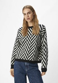 Stickad tröja med ett svart och vitt zigzag-mönster. Rund halsringning och ribbade ärmslut. Kombinerad med strukturerade blå jeans.