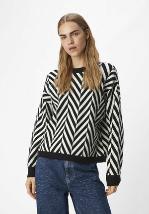 Maglione a maglia con un motivo a zigzag bianco e nero. Collo rotondo e polsini a coste. Abbinato a jeans blu con texture.