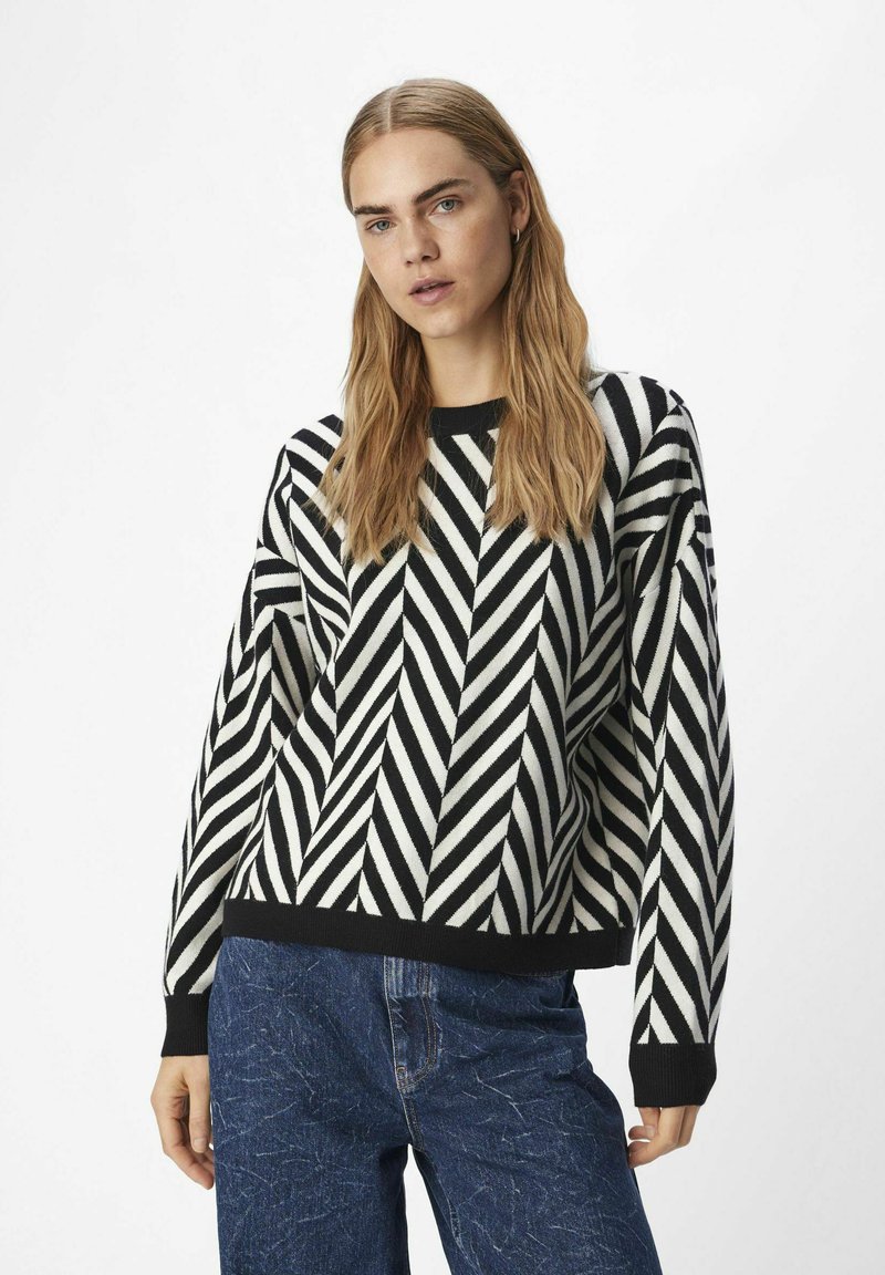 Stickad tröja med ett svart och vitt zigzag-mönster. Rund halsringning och ribbade ärmslut. Kombinerad med strukturerade blå jeans.