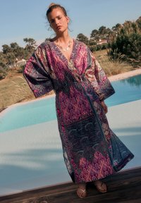 Kaftan lung, vaporos, cu un model vibrant paisley în roz, albastru și verde. Confecționat dintr-un material ușor, cu mâneci largi și talie cu centură.