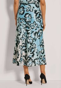 Blumiger Midirock in Hellblau und Schwarz, mit großen Blumenmustern, ausgestelltem Schnitt und weicher Textur, kombiniert mit schwarzen High Heels.