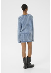 Robe en maille torsadée bleu clair, avec une coupe ample, des poignets et un ourlet côtelés. Associée à des bottines noires pour un contraste.