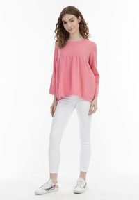 Top rosa strutturato con maniche lunghe, caratterizzato da una vestibilità comoda e dettagli arricciati sul busto, abbinato a jeans skinny bianchi e sneaker colorate.