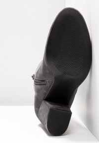 Bottine en suède gris avec un talon carré, une fermeture éclair sur le côté et une semelle en caoutchouc noir texturé. Tige lisse avec une finition mate.