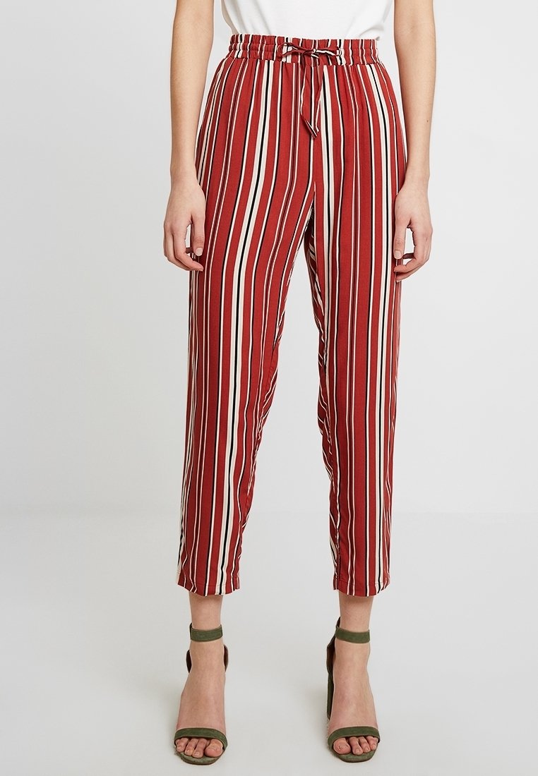 Pantalon à rayures rouges et blanches avec une coupe décontractée, une taille élastique et un détail noué, longueur raccourcie et texture de tissu lisse.