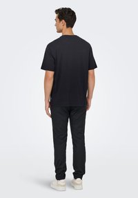 Sort bomuld t-shirt med rund hals, korte ærmer og afslappet pasform, kombineret med sorte bukser og lyse sneakers. Minimalistisk design.