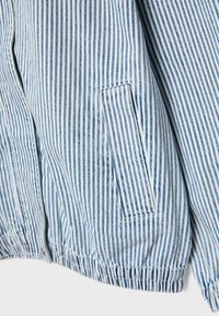 Tissu rayé verticalement bleu et blanc avec une petite poche rectangulaire et un ourlet élastiqué, partie d'un vêtement.