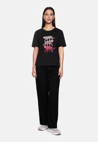 Black t-shirt featuring a graphic of stacked leopards in pink and white. Paired with black loose-fitting trousers and light sneakers.