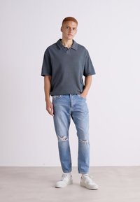 Polo grigio scuro con maniche corte e sottili righe, abbinato a jeans strappati blu chiaro e sneaker bianche.