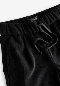 Sorte ribbede joggers med elastisk talje, snøre og tekstureret stof. Har et lille mærke på taljen.
