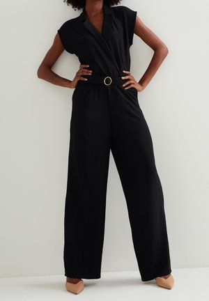 Schwarzer Jumpsuit mit kurzen Ärmeln, Wickeldesign und Gürtel mit goldener, runder Schnalle. Weite Hosenbeine und strukturierter Stoff.