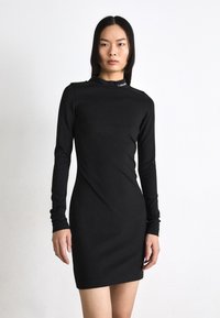 Long-sleeve black dress made of smooth fabric, featuring a high neck and a small logo detail at the collar. Fitted silhouette and above-knee length.