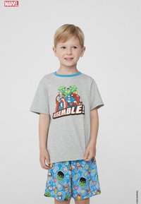 Graues T-Shirt mit blauem Halsauschnitt, das ein Superhelden-Design zeigt, kombiniert mit blauen Shorts, die verschiedene Charaktergesichter und Symbole zeigen.