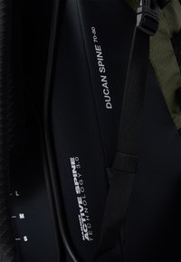 Interior de una mochila de senderismo negra y verde que muestra las etiquetas "DUGAN SPINE 70-80" y "ACTIVE SPINE TECHNOLOGY 3.0" con correas ajustables.