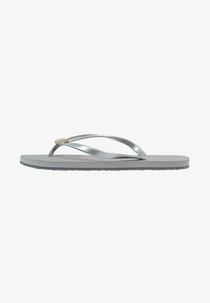 Sandale tongs argentée avec semelle texturée et fines brides, montrée de profil sur fond blanc.