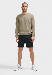 Beige crewneck sweatshirt med en strukturerad design, kombinerad med svarta shorts och vita sneakers med svarta detaljer.