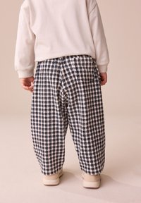 Pantalon ample à carreaux bleu marine et crème avec un tissage texturé. Taille élastique et poches latérales, associé à des chaussures légères.