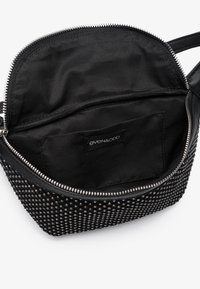 Borsa nera con chiusura a zip e esterno borchiato. All'interno presenta una fodera in tessuto con una piccola tasca e un'etichetta di marca.