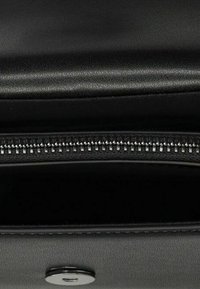 Interiér černé kožené tašky s uzavíráním na zip a stříbrným kováním. Hladká textura s jednou otevřenou přihrádkou a bez viditelných vzorů.