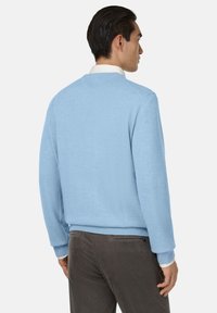 Lichtblauwe trui met een ronde hals en ribgebreide manchetten en zoom, gedragen over een witte overhemd met kraag. Soepele textuur en een ontspannen pasvorm.