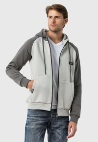 Reißverschluss-Hoodie in Hellgrau und Dunkelgrau, hergestellt aus einem weichen Baumwollmischgewebe. Verfügt über eine große Fronttasche und eine Kapuze mit Kordelzug.