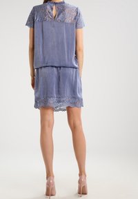 Vestido azul claro con detalles de encaje en la parte posterior y el dobladillo, que presenta un escote con abertura, mangas cortas y un ajuste relajado.