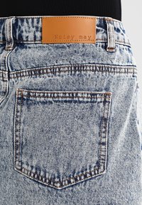 Jeans de mezclilla en azul claro con desgaste, que presentan una etiqueta de cuero marrón grabada con "Noisy May" en la cintura y en un bolsillo trasero.