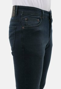 Donkerblauwe denim jeans met een aansluitend ontwerp, voorzien van gestikte details, koperkleurige hardware en een leren label op de tailleband.