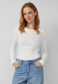 Maglietta bianca a maniche lunghe con scollo rotondo, abbinata a jeans azzurri chiari. Presenta un design aderente e una texture morbida.