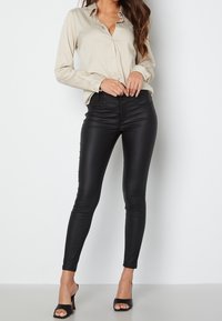 Chemise beige à manches longues avec boutons, pantalon skinny taille haute noir en similicuir, talons bloc transparents, texture lisse, coupe ajustée.