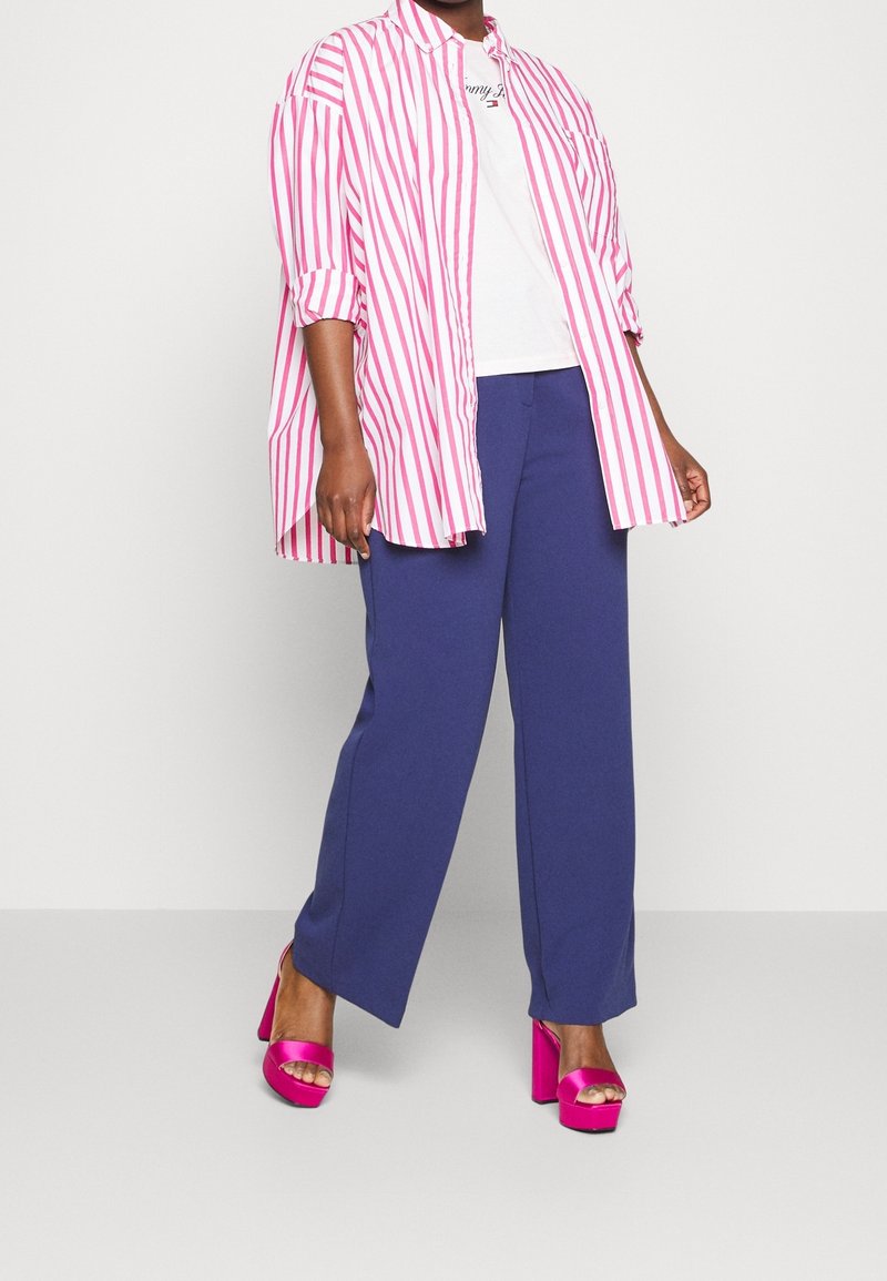 Camisa de rayas rosa y blanca de gran tamaño, camiseta blanca debajo, pantalones de pierna ancha azul marino y tacones de plataforma rosa vibrante.