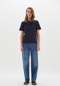 Jūrų mėlynos spalvos crew-neck marškinėliai trumpomis rankovėmis, derinami su aukštu liemeniu, plačiais mėlynais džinsais ir juodais sandalais. Paprastas dizainas, minimalistiškas stilius.