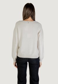 Pull crème à coupe décontractée, avec un ourlet côtelé et des manches longues, présentant un détail scintillant subtil sur une texture lisse. Porté avec un jean foncé.
