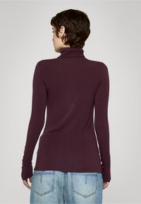 Burgunderfarget turtleneck-genser med lange ermer, myk tekstur og smal passform. Kombinert med lyseblå, løstsittende denimjeans.