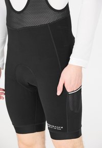 Shorts de cyclisme noirs avec une partie supérieure en mesh, insert rembourré, et une poche latérale avec un motif texturé. Marquage sur la partie inférieure de la jambe.