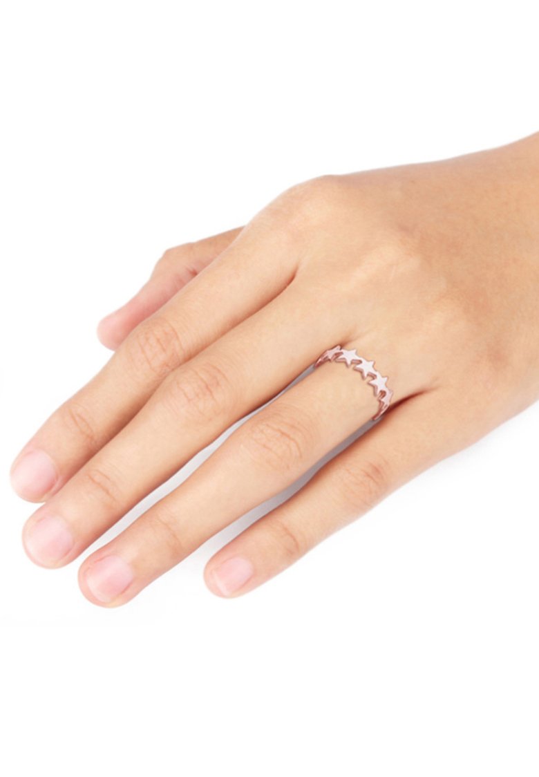 Anillo de oro rosa con un diseño ondulado y formas de estrellas, colocado en una mano con uñas naturales y sin pulir.