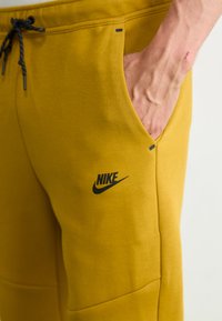 Nike-Sweatpants in Senfgelb, mit Logo, Seitentasche, Kordelzug und glattem Baumwoll-Mischmaterial.