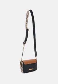 Crossbody bag featuring a black body, tan flap, and a snake-print strap. Gold hardware accents complete the design.