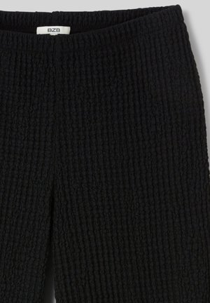 Jupe en maille noire texturée avec fente avant et taille élastique, avec une petite étiquette blanche portant les initiales de la marque BZB.