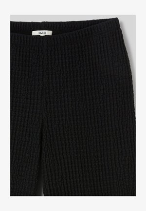 Jupe en maille noire texturée avec fente avant et taille élastique, avec une petite étiquette blanche portant les initiales de la marque BZB.