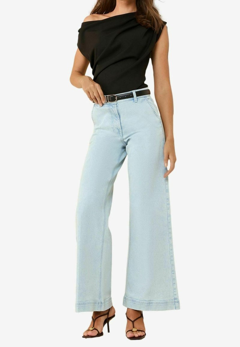 Černý top s odhalenými rameny, světle modré široké džíny páskované v pase, s hrubým lemem a odřeninami. Černé sandály na pásky.