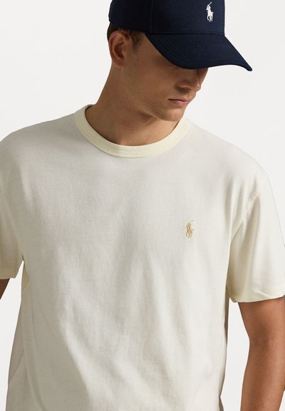 T-shirt creme de mangas curtas com um colarinho leve e texturizado, e um pequeno logótipo bordado no peito. Material em mistura de algodão, textura suave.