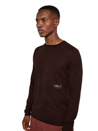 Mann trägt ein eng anliegendes dunkelbraunes Langarmshirt mit „HALO“-Logo auf der Brust, kombiniert mit bordeauxfarbenen Hosen, blickt nach links vor weißem Hintergrund.