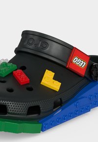 Μαύρο παπούτσι Crocs με υπερμεγέθη μπλε και πράσινα κομμάτια στην σόλα και κίτρινα, κόκκινα και πράσινα LEGO τουβλάκια προσαρτημένα στην κορυφή.