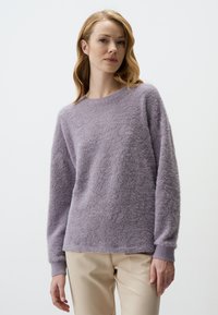 Lila losse trui gemaakt van fluffy breiwerk. Heeft een ronde halslijn en lange mouwen, gecombineerd met licht beige broeken.