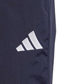 Pantalones deportivos en color marino con un destacado logo bordado de tres franjas en blanco. Tela sintética suave con un corte ajustado.