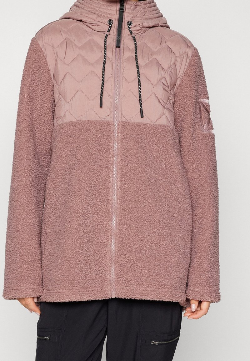 Veste à capuche mauve clair avec partie supérieure matelassée et partie inférieure en polaire texturée, fermeture éclair frontale et cordons noirs sur la capuche.