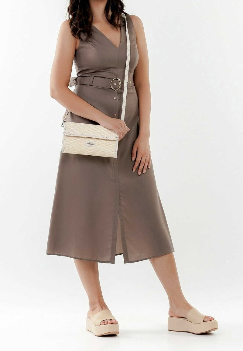Abito marrone senza maniche con scollatura a V e bottoni frontali, abbinato a una borsa a tracolla crema e sandali con zeppa beige.