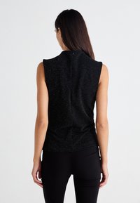 Top negru fără mâneci, cu un finisaj texturat, având sclipiri discrete și guler înalt. Spatele are un fermoar ascuns și un design mulat.