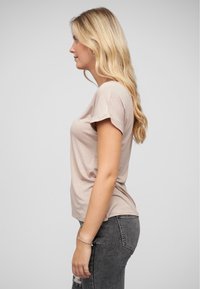 T-shirt courte couleur beige clair avec une coupe décontractée, texture lisse et drapé subtil, associé à un jean gris foncé déchiré.